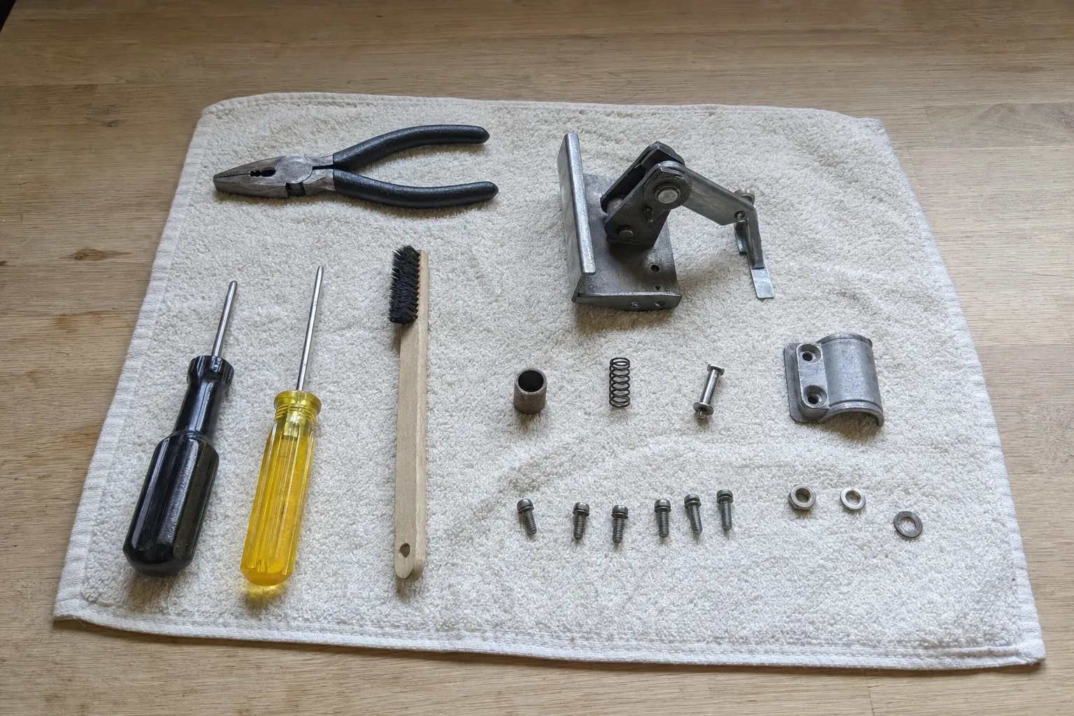 Appliance door hinge, spring and fixings laid out on a cloth with screwdrivers, pliers and a parts brush
